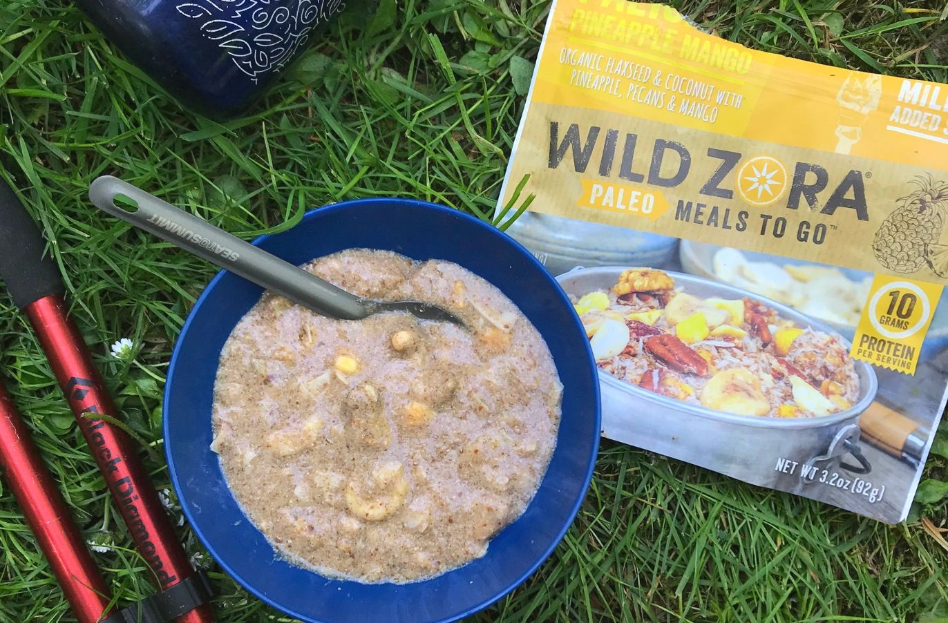 Wild Zora paleo meals to go package beside a bowl of paleo porridge on a grassy surface