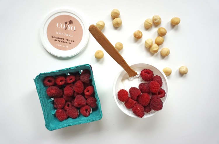 container of coyo with raspberries beside a container of raspberries beside macadamia nuts