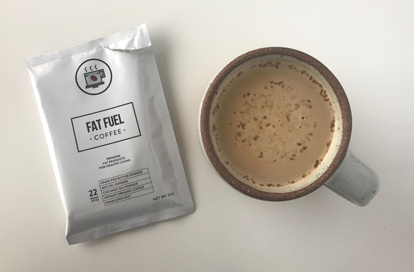 a packet of fat fuel coffee next to a mug of Keto Coffee on a white surface