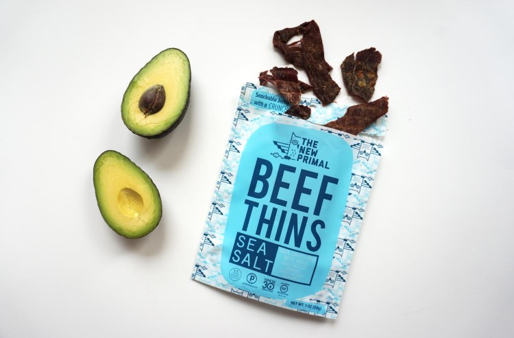 two halves of an avocado next to a bag of the new primal beef thins
